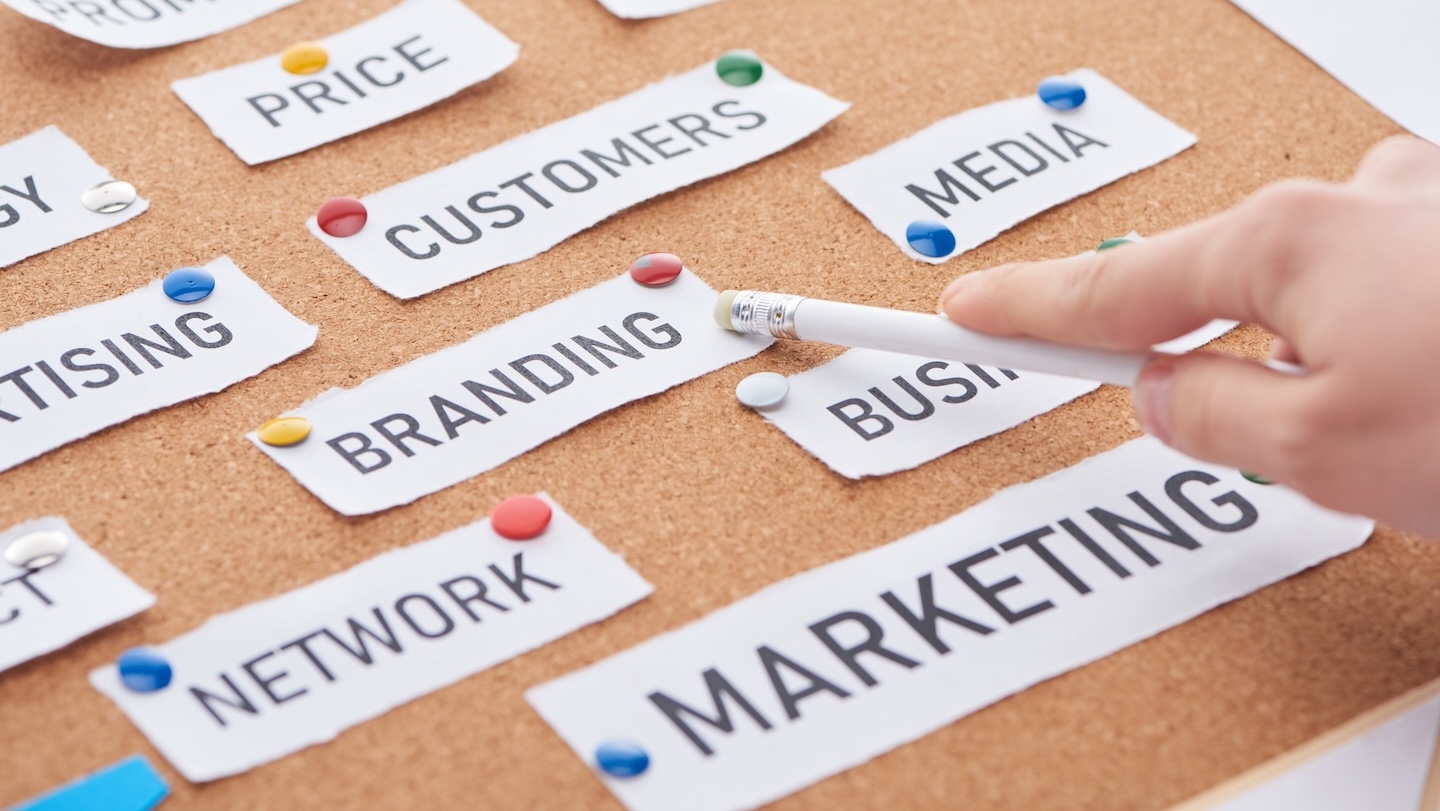 cropped view of woman pointing with pencil on branding inscription on cork board